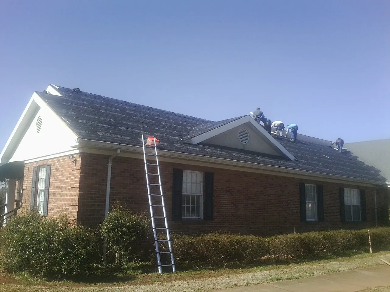 Crew tearing shingles off a brick ranch roof with a ladder set — Emergency Roof Repair work by our crew in Trumbull
