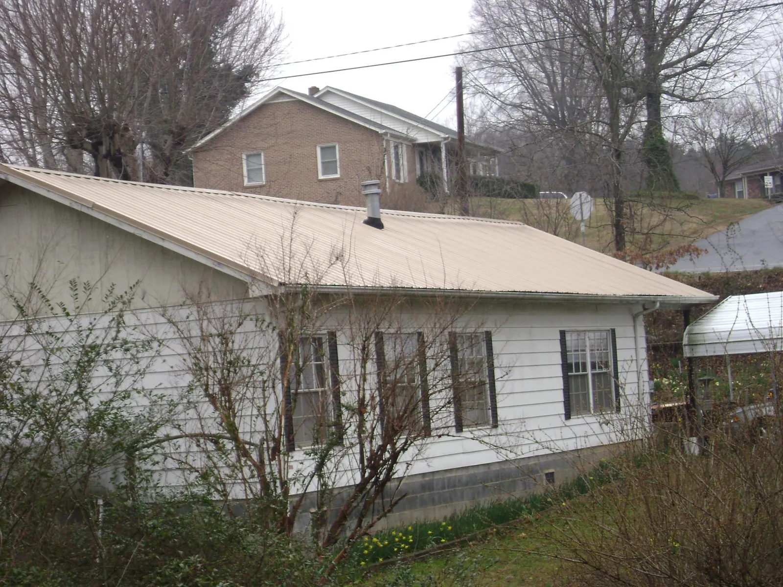 Tan metal roof on a white sided house set into a hillside — Commercial Roofing by Roofing Brothers in Trumbull