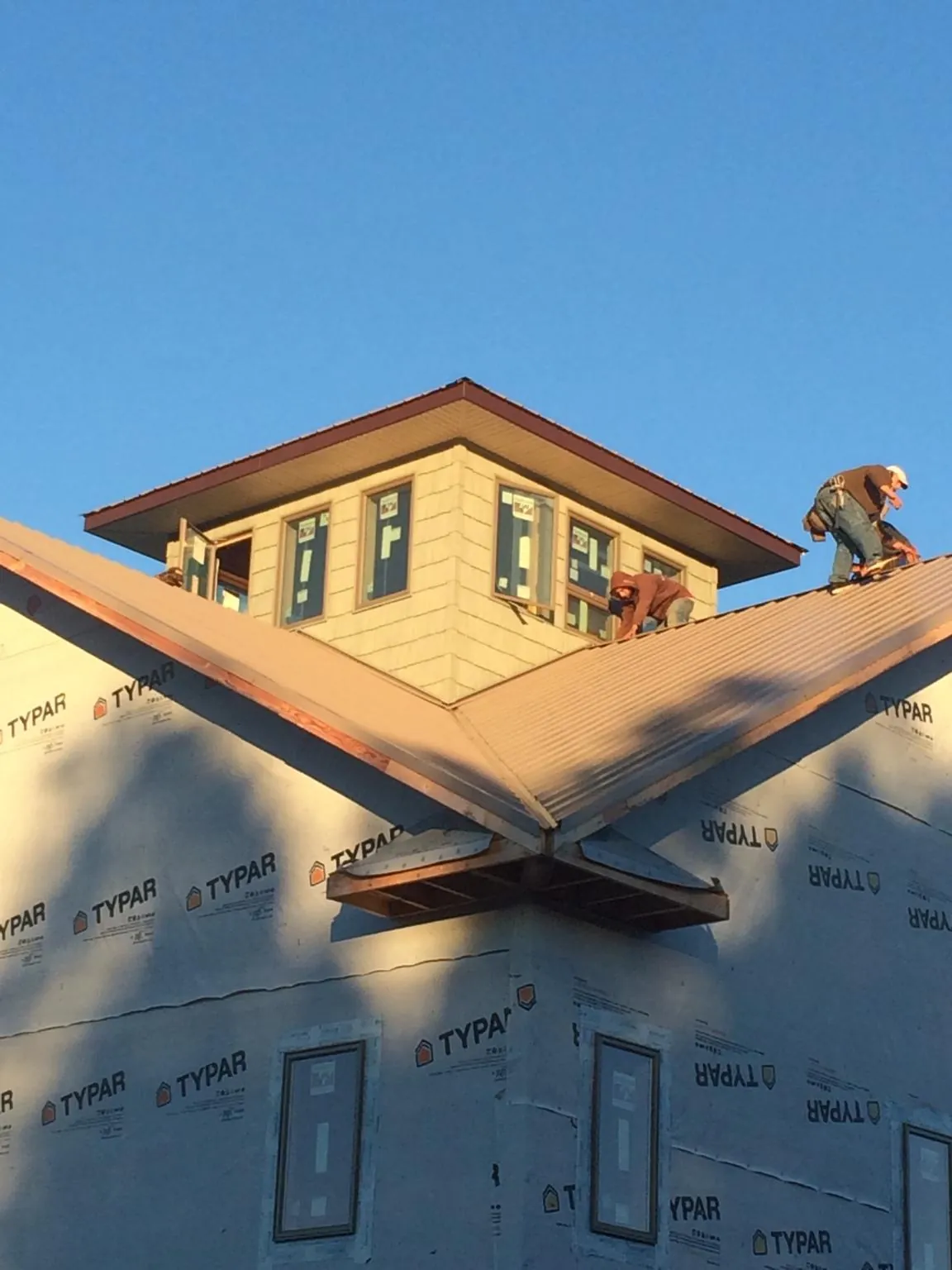 Roofers working around a rooftop cupola on a new metal roof at sunset — Roof Waterproofing in Trumbull by Roofing Brothers